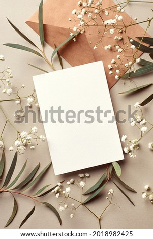 Invitation or greeting card mockup with craft paper envelope, eucalyptus and gypsophila twigs. Card mockup with copy space on beige background. Royalty-Free Stock Photo #2018982425