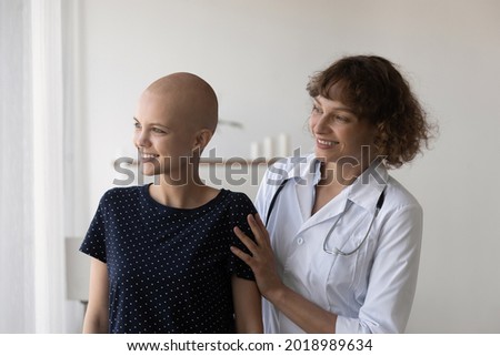 Compassionate kind young female doctor therapist oncologist giving psychological support to smiling hairless woman, telling effective good treatment news, visualizing healthy future together indoors. Royalty-Free Stock Photo #2018989634