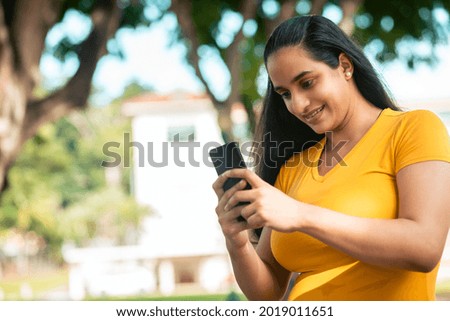 A closeup shot of a Hispanic woman looking at her phone and smiling