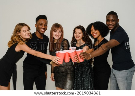 Waist up of six friends having fun and drinking alcohol during New Year party, isolated on white background. A group of cheerful friends of different nationalities clink glasses with red glasses at a