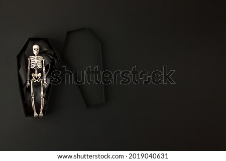 Toy skeleton of man in papercraft coffin on black background, Stylish monochrome Halloween concept, creative idea, banner, flyer, invitation for night party, minimal handmade decor