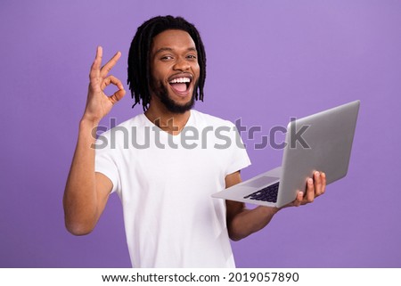Photo of happy brunette braids haired man wear white t-shirt hold laptop show okay sign isolated on violet color background