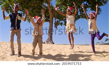 Happy Indian female and male kids celebrating New Year in Santa Claus hats on a beach