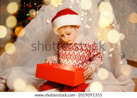 Merry Christmas. Happy child with magic gift near Xmas tree. Family enjoying Christmas. Happy childhood concept. Little happy boy find gifts near Xmas tree. Discover beauty of winter. Cozy interior