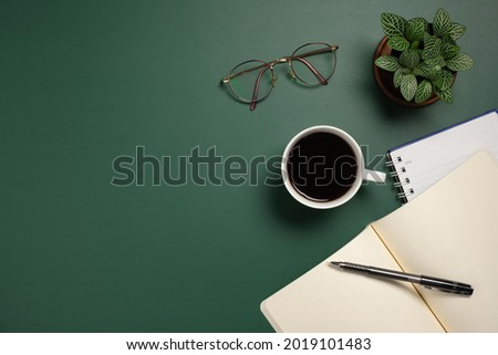 Desk office with blank document, flower, coffee cup, glasses and pen on green table. Flat lay top view copy space.