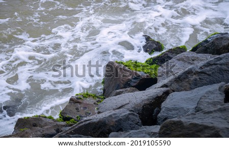 Ocean waves crashing onto the rocks, green algae growing on the rocks.