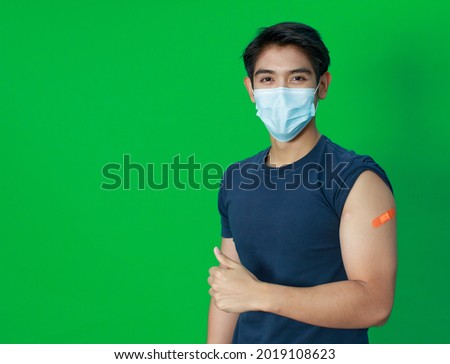 Asian young man wearing protective hygiene mask trust and confident show arms with bandage plaster after getting Coronavirus or Covid-19 vaccine injection. Idea for safe and drug allergy free.