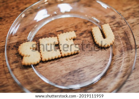 Inscription made of cookies "SEE YOU" Plate with alphabet Biscuits on wooden table with bluer background. Top view photo.