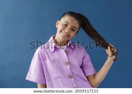 Smiling, positive teenage girl playing with her hair on a blue background. The girl is posing