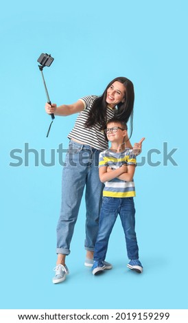Young woman and her little son taking selfie on color background