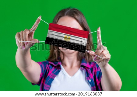 Woman in a plaid shirt holds a medical mask with of the Egypt flag on a green background