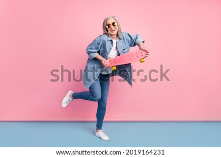 Full body photo of crazy elder lady hold skate go wear spectacles jeans shirt isolated on pink background