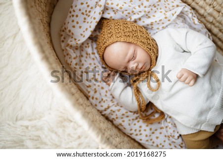 A reborn newborn baby doll toy dressed in a mustard colored bonnet hat and a white cardigan lying in a cream moses basket bassinet - infant is a doll
 Royalty-Free Stock Photo #2019168275