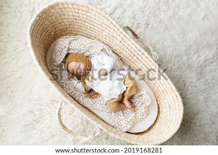 A reborn newborn baby doll toy dressed in a mustard colored bonnet hat and a white cardigan lying in a cream moses basket bassinet - infant is a doll
 Royalty-Free Stock Photo #2019168281