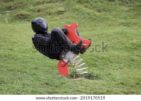 motorcyclist in black motorcycle clothing is sitting on a rocking horse on children's playground and is going crazy Royalty-Free Stock Photo #2019170519