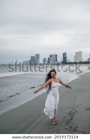 Beautiful young asian woman in white dress walking with hands to the side on the beach. Romantic and peaceful photo.