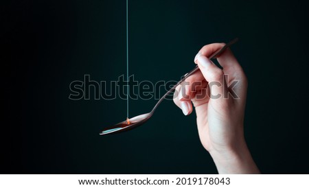 Female Caucasian Hand Holding a Spoon With Yellow Golden Liquid Dripping on it in an Artsy Way on a Black Background.