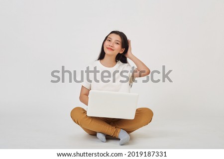 Smiling Asian woman working on laptop computer while sitting on the floor with legs crossed isolated over white ​background, Back to school concept