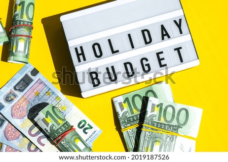 Lightbox board with word HOLIDAY BUDGET on yellow background around euro banknotes. Money, Business, finance, investment, saving. Cash bill. Business budget of wealth and prosperity finance. Passive 