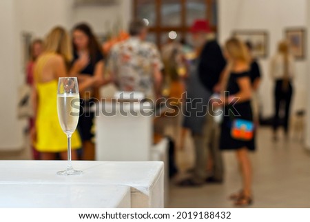 Glasses with wine on the background of the exhibition of paintings. People blurred in the background. Art salon with white walls.