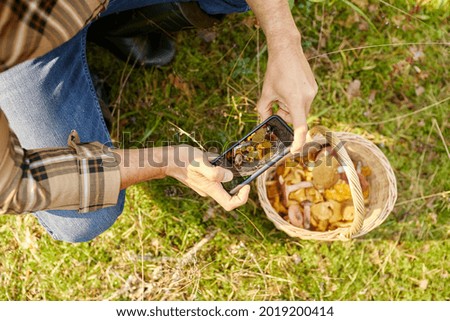 picking season and leisure people concept - middle aged man with smartphone and mushrooms in basket in autumn forest