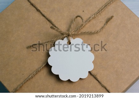 Gift box tied with a jute rope in rustic style, with a white tag, on a light wooden background, place to insert text and copy space