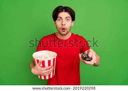 Photo of speechless stunned guy hold popcorn box remote control wear red t-shirt isolated green color background
