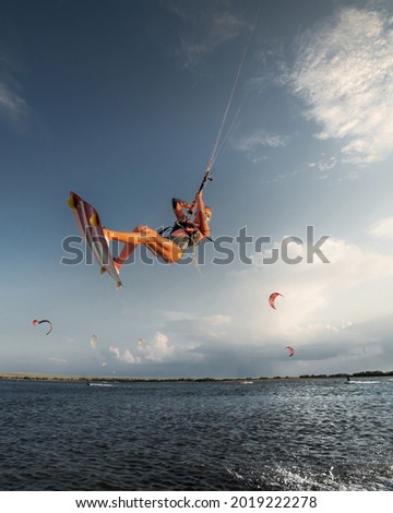 Professional athlete kitesurfer young caucasian woman doing a trick in the air against the backdrop of the sunset sky and clouds. Professional kitesurfing and kite culture training Royalty-Free Stock Photo #2019222278
