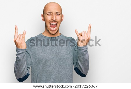 Bald man with beard wearing casual clothes shouting with crazy expression doing rock symbol with hands up. music star. heavy concept. 