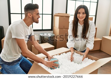 Young hispanic couple smiling happy unpacking cardboard box at new home.