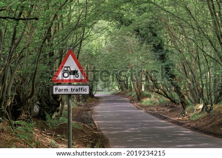 A red and white coloured triangle farm traffic warning sign with an image of a tractor on a country lane in the English countryside