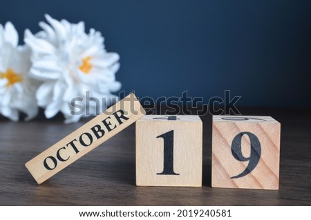 October 19, Date cover design with calendar cube and white Paeonia flower on wooden table and blue background.