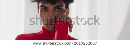 african american man with hand near face looking at camera on background with white drapery, banner