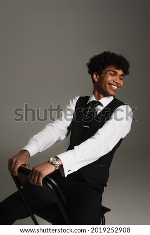 elegant african american man smiling with closed eyes while sitting isolated on grey