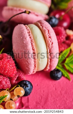 Square pink cake garnished with macarons and fresh berries. Cake for the holiday. Dessert is garnished with fresh raspberries, white currants, cherries and blueberries.