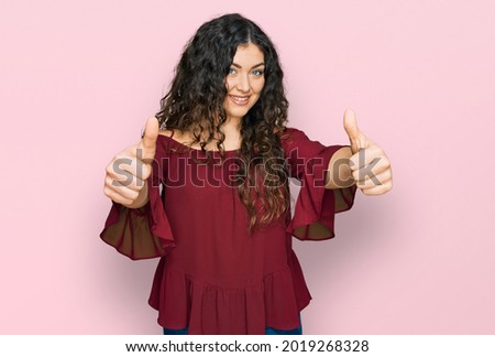 Young hispanic girl wearing casual clothes approving doing positive gesture with hand, thumbs up smiling and happy for success. winner gesture. 