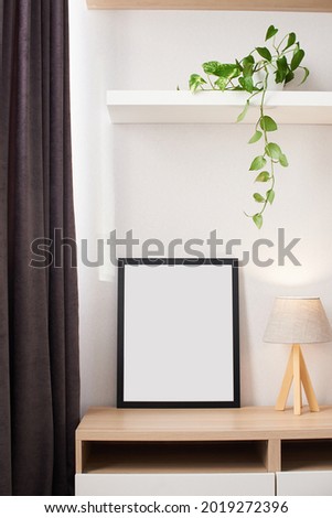 Empty photography frame mock up with wooden lamp and lush plant on shelf. Template for pictures, photos. Home interior, domestic room in black and white colors with wooden elements and flower.