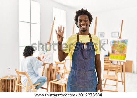 African young man standing at art studio showing and pointing up with fingers number four while smiling confident and happy. 