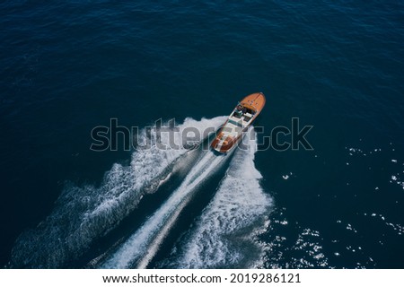 Top view of a wooden powerful motor boat. Classic Italian wooden boat fast moving aerial view. Luxurious wooden boat fast movement on dark water. Royalty-Free Stock Photo #2019286121