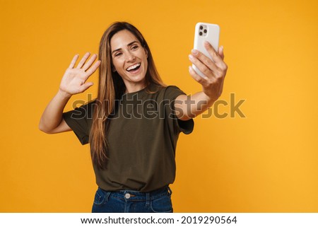 Happy mid aged casual woman taking selfie with mobile phone while standing over orange background waving