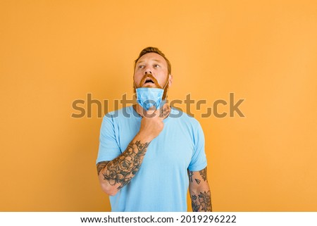 man with beard and tattoos removes the mask for covid-19 Royalty-Free Stock Photo #2019296222