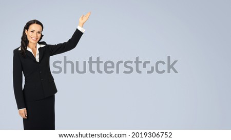 Photo image of happy smiling attractive woman in black confident suit, showing advertising mock up copy space. Business concept. Isolated over grey background. Brunette businesswoman. Female model.