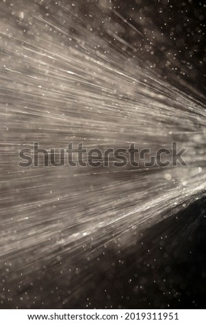 Vertical view of gushing water flying rapidly across frame, against dark background and intentional motion blur. Full frame photo of water jet floating mid air under afternoon sunlight