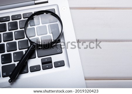 Magnifying glass laying on a laptop keyboard. Technology file search tool concept, data forensics, computer crime and device investigation, closeup Royalty-Free Stock Photo #2019320423
