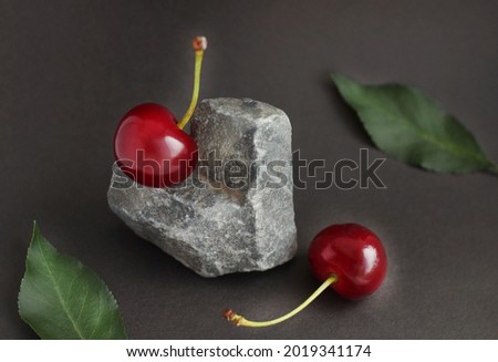 Cherry berries located on a stone in the form of a heart, and cherry leaves on a dark background