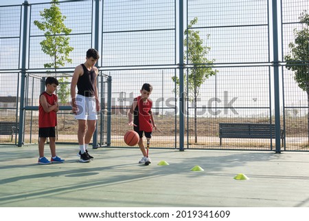 Basketball trainer teaching two children how to play basketball, one of them has a leg prosthesis. Coach training two kids.