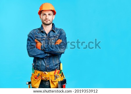 Portrait of confident handsome male construction worker with crossed arms and copy space staying over blue background looking to camera Royalty-Free Stock Photo #2019353912