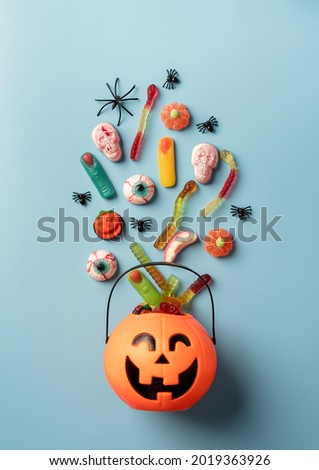 Halloween concept. Various halloween sweets in a pumpkin pot top view on blue solid background. Halloween party greeting card mock up
