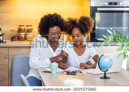 African American mother is teaching her daughter are using laptop at home together. Mother and daughter studying with laptop. Woman and child using a laptop together 