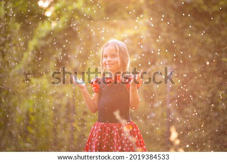 Beautiful little blonde girl, has happy mood, fun smile, enjoy rain in nature garden. Child portrait. Lifestyle instagram concept. Summer time. Fashion kid style. Amazing face.